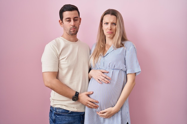 Young couple expecting a baby standing over pink background depressed and worry for distress crying angry and afraid sad expression