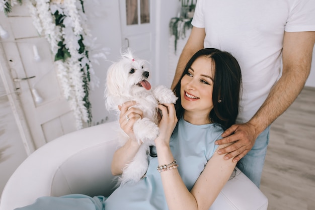 Young couple expecting baby with a dog standing together indoors