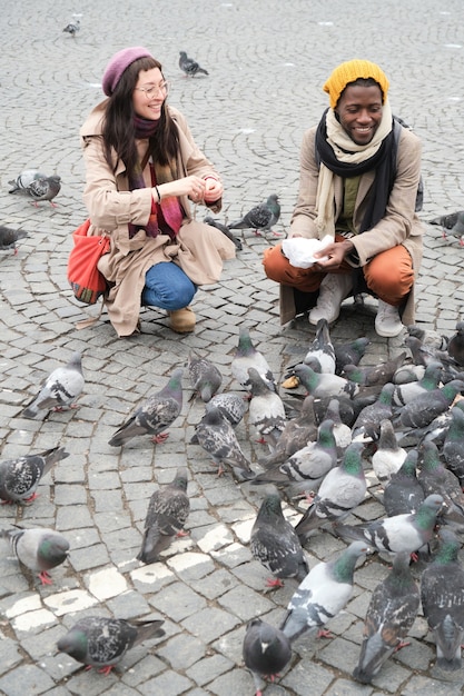 Young couple feeding birds together during their walk in the city