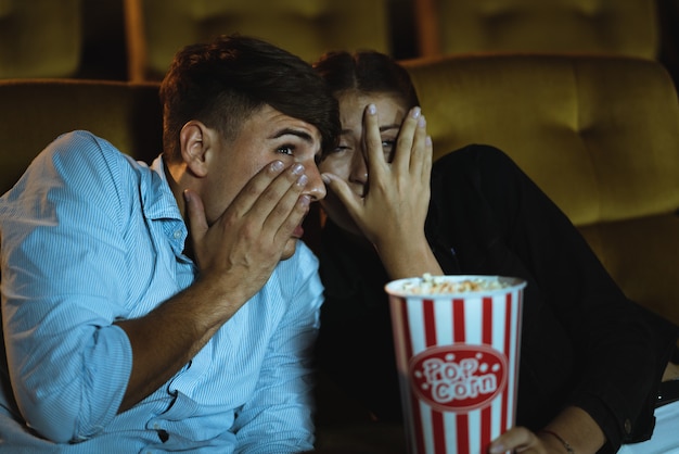 映画館でホラー映画を見ながら手を怖がらせる若いカップルが手を上げる