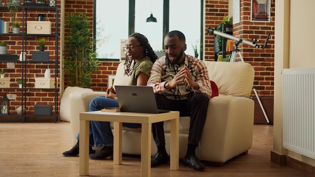 Young couple fighting and being angry about difficulties, having relationship issues sitting on sofa at home. Angry man and woman yelling, having argument and acting furious or annoyed.