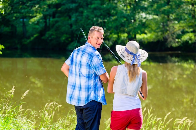 Young couple fishing or angling standing on river shore in grass