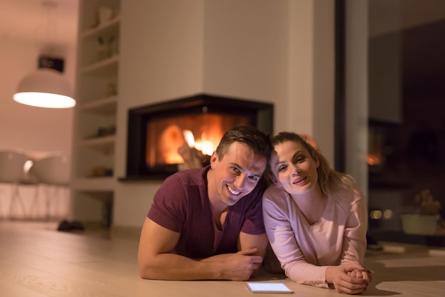 Young Couple on the floor in front of fireplace surfing internet using digital tablet on cold winter night