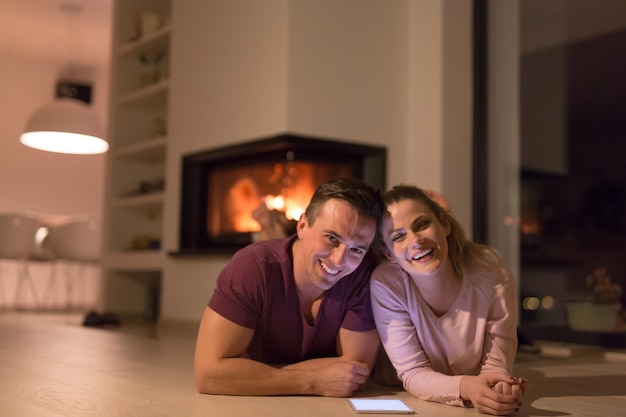 Young Couple on the floor in front of fireplace surfing internet using digital tablet on cold winter night