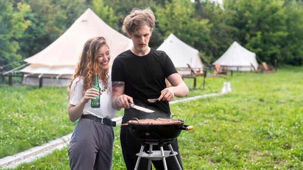 写真 グリルで肉を揚げ、背景にビールのテントを飲む若いカップル