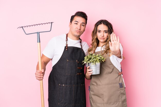 Young couple gardener isolated standing with outstretched hand showing stop sign, preventing you.