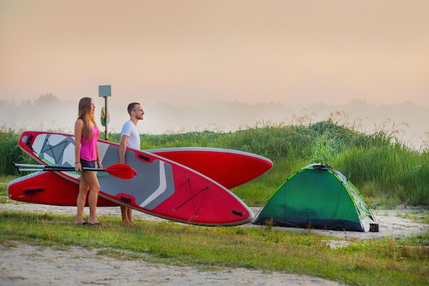 Young couple go with surfboards to the water tourism and active recreation