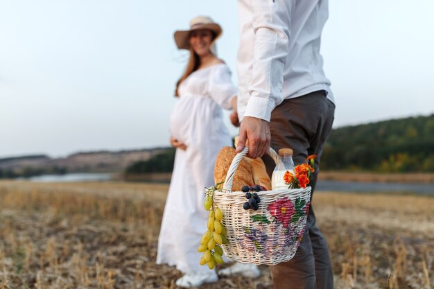 Photo young couple goes on a picnic in the field, the guy carries a basket with fruits, milk and bread