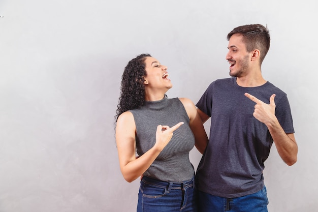 Young couple on gray wall pointing.