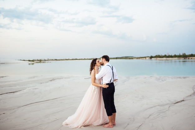 Young couple a guy in black breeches and a girl in a pink dress are walking along the white sand of the desert