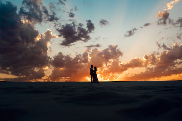 Foto la giovane coppia un ragazzo in calzoni neri e una ragazza in un vestito rosa stanno camminando lungo la sabbia bianca del deserto