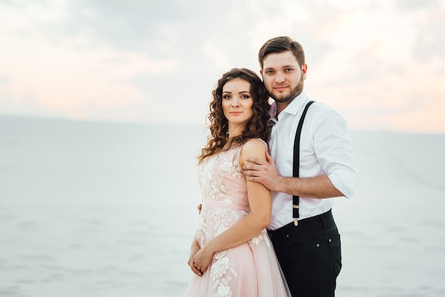 Young couple a guy in black breeches and a girl in a pink dress are walking along the white sand of the desert