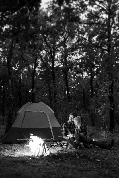 Young couple a guy and a girl in bright knitted hats stopped at a camping near the fire