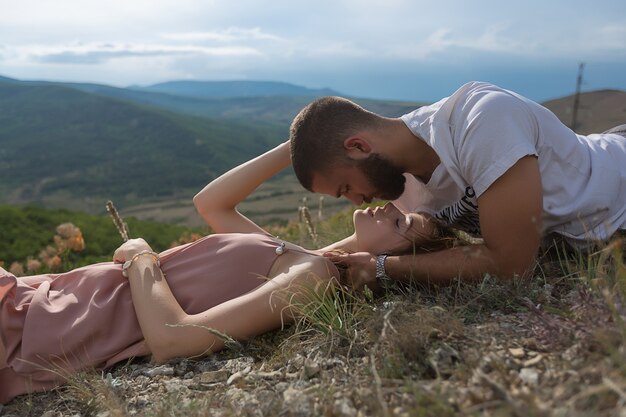 Foto una giovane coppia ragazzo e una donna giacciono sull'erba e si guardano contro le alte montagne e il cielo blu. natura meravigliosa.