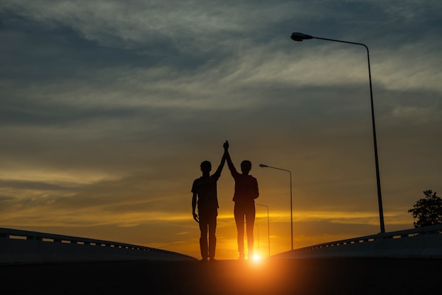 Young couple hand up at sunset on the road.