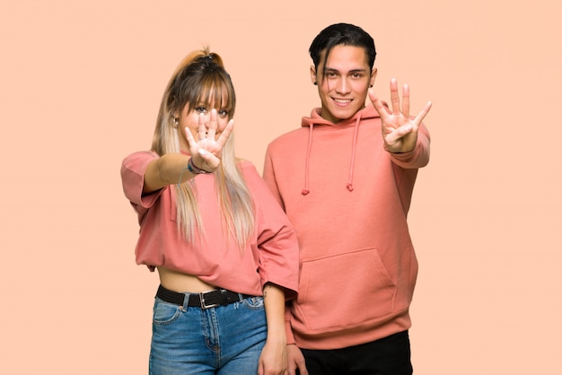 Young couple happy and counting four with fingers over pink background