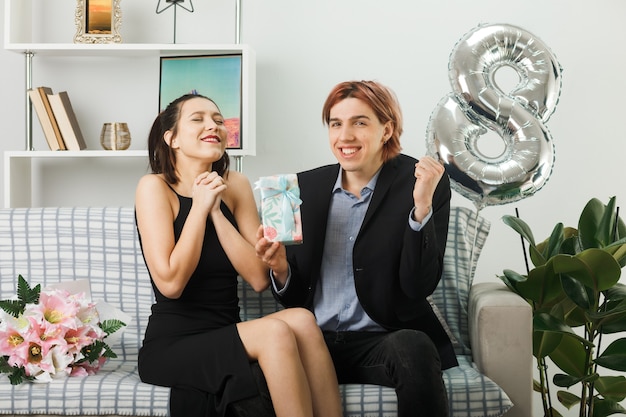 Young couple on happy women day holding present sitting on sofa in living room