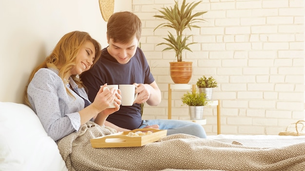 Photo young couple has breakfast in bed drinks tasty coffee miling in bedroom, sunlight