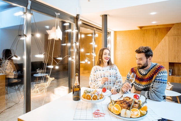 Young couple having festive dinner sitting together in the modern house during the winter holidays