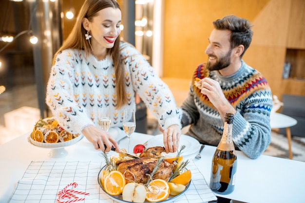 Young couple having festive dinner sitting together in the modern house during the winter holidays