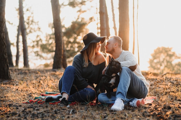 Young Couple Having Fun with Their Dog french bulldog at Sunset Outside of City on the Nature