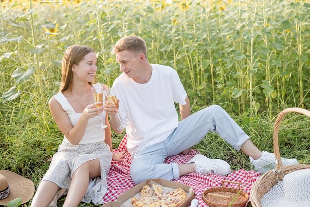 Young couple having picnic on sunflower field at sunset