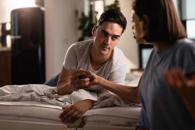 Young couple having relationship problems and arguing over mobile phone in the bedroom Focus is on man