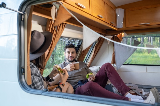 Young couple having tea with sandwiches in house on wheels