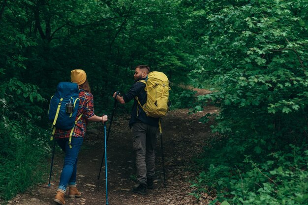 A young couple of hikers using trekking poles and wearing\
backpacks