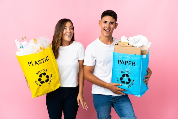 Young couple holding a bag full of plastic and paper on pink with surprise facial expression