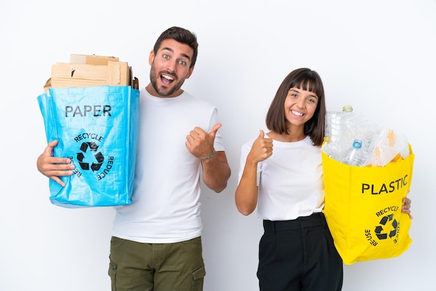 Young couple holding a bag full of plastic and paper to recycle isolated on white background giving a thumbs up gesture with both hands and smiling