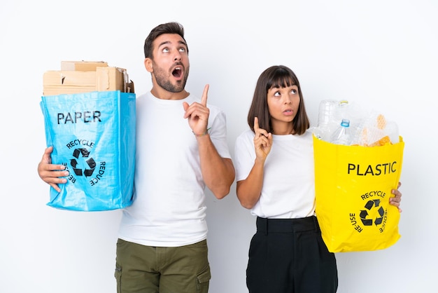 Young couple holding a bag full of plastic and paper to recycle isolated on white background thinking an idea pointing the finger up