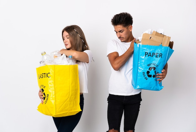 Young couple holding a bag full of plastic and paper on white suffering from pain in shoulder for having made an effort