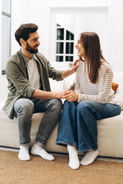 young couple holding hands and talking on sofa at home
