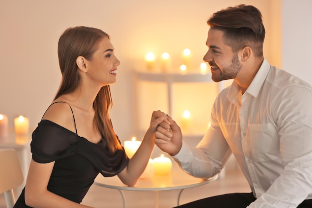 Young couple holding hands while sitting at table with burning candles