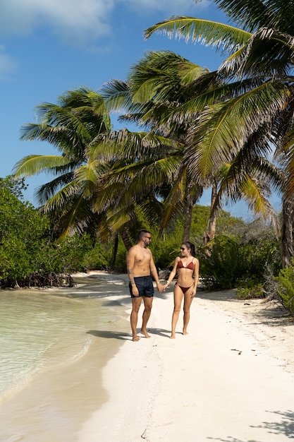 Foto una giovane coppia si tiene per mano mentre cammina lungo la riva del mare in un luogo idilliaco in messico isla contoy