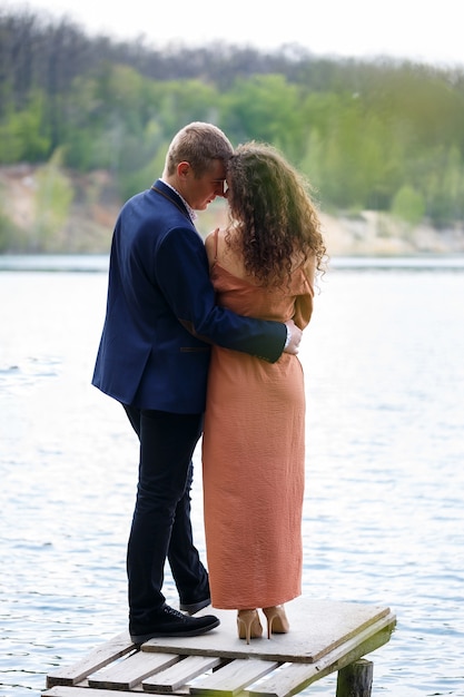 A young couple holding hands on a wooden bridge in the middle of a blue lake. Masonry on the island on a background of trees. Nature, landscape. Romance and love, happy couple