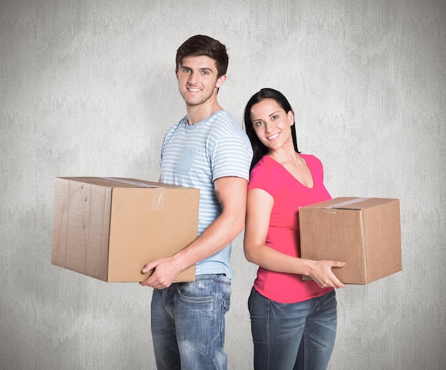 Young couple holding moving boxes against weathered surface