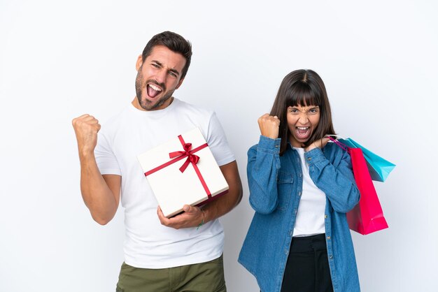 Young couple holding shopping bags and present isolated on white background celebrating a victory