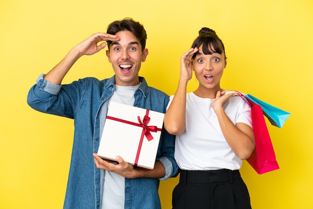 Young couple holding shopping bags and present isolated on yellow background has just realized something and has intending the solution