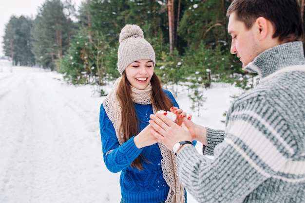 Young couple holding snow heart in winter forest. Hands in knitted mittens with heart of snow in winter day.