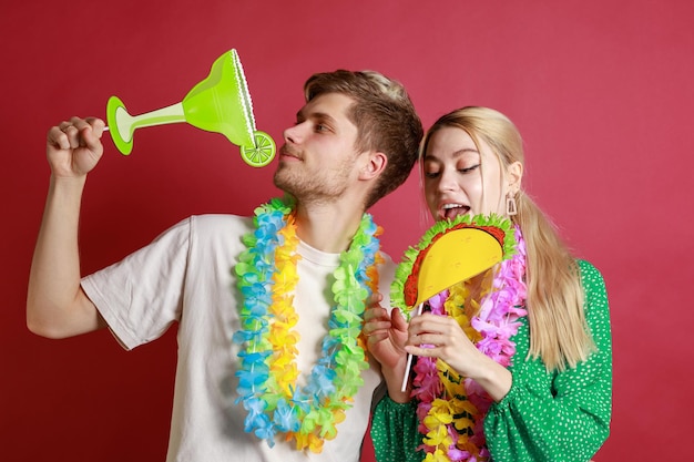 Young couple holding tequila and taco boards and standing on red background