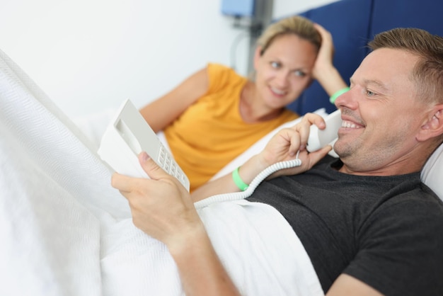 Photo young couple in hotel room on bed calls the receptionist on phone hotel service concept