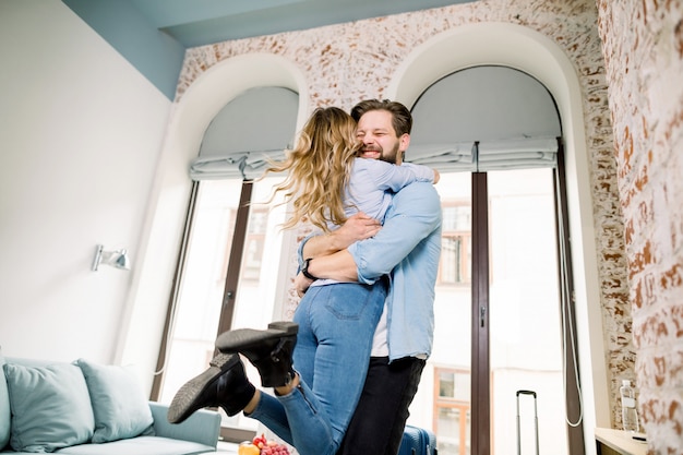 Young Couple at Hotel Room. Happy young couple hugging and smiling while standing in modern hotel room