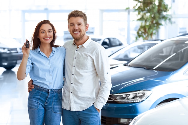 young couple hugging in a car salon showing car keys to a newly bought vehicle