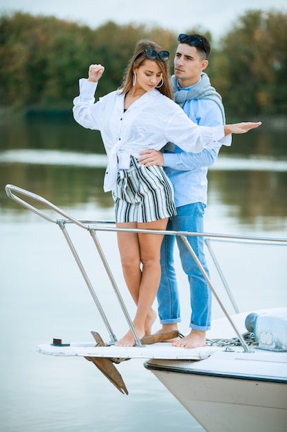 Young couple hugging on deck of sailboat. Romantic couple on a pleasure boat. Happy wealthy man and a woman by private boat have sea trip. Couple on honeymoon traveling with yacht
