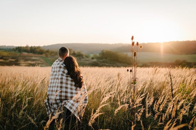 Young couple hugging, standing back, people covered with blanket, at sunset in autumn an outdoor