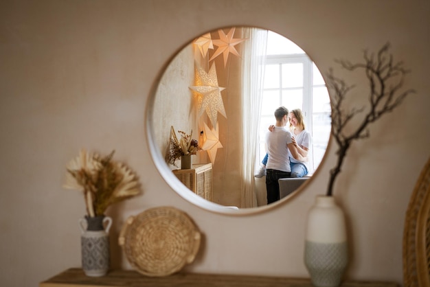 Young couple hugging while sitting on windowsill by window in casual clothes view reflected in the m...