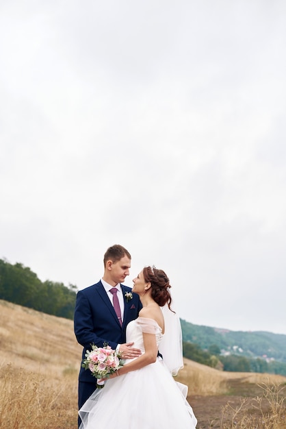 A young couple hugs in a field next to the river on their wedding day. Happy couple. Wedding photo. Couple in love.