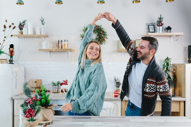 若いカップルの夫と妻は新年とクリスマスのお祝いの準備を幸せ、家族はキッチンで踊って楽しんでいます